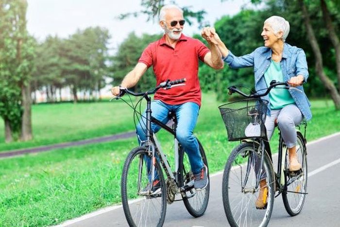 Happy senior couple over 60 riding bikes and holding hands in park, joyful mature pair sharing outdoor life, sincere companionship for singles over 50