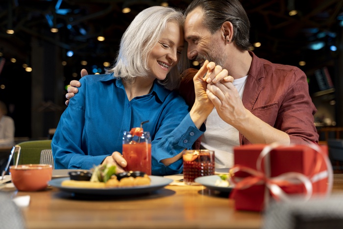  Senior man surprising his friend with a present at a restaurant