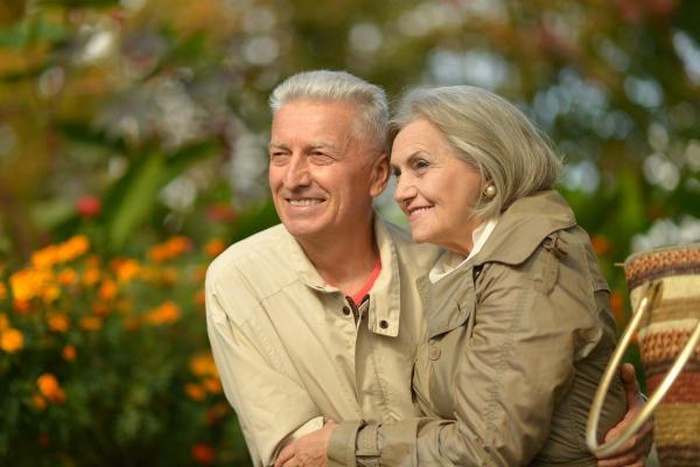 Affectionate elderly couple embracing outdoors among vibrant garden flowers