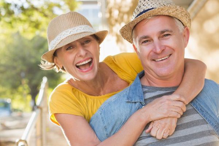 Joyful mature Caucasian couple wearing straw hats embracing outdoors
