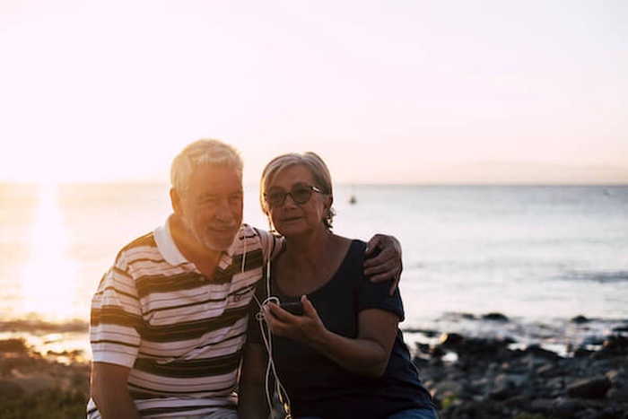 Portrait of man and woman listening music while sitting at beach against clear sky