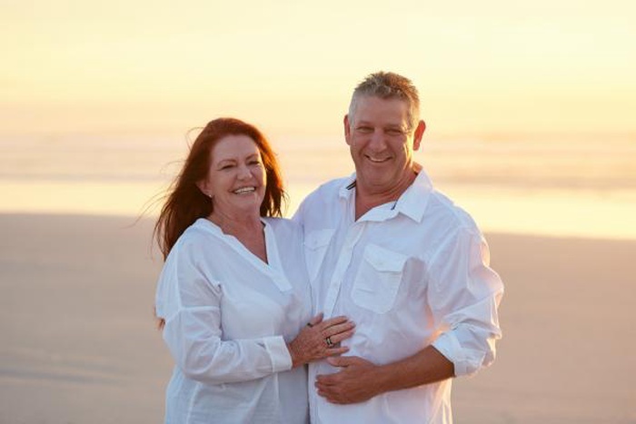 Loving mature couple embracing warmly on the beach during golden sunset, smiling happily