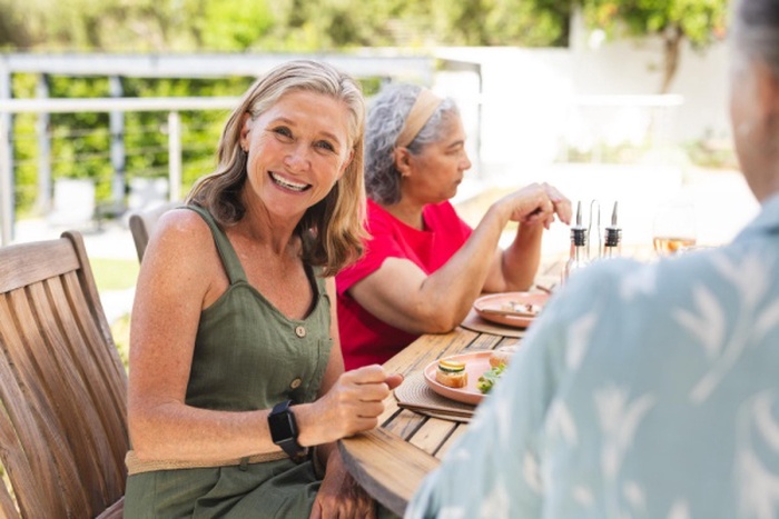 Diverse senior female friends wearing green dining outdoors