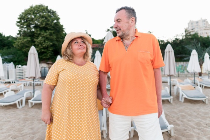 Front view of elder tourist couple on beach holding hands
