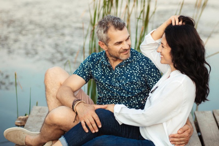 A mature married couple are sitting by the lake and hugging happy lovers 50 years old