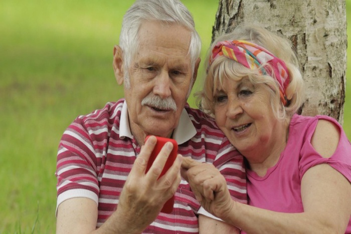 Family picnic senior old grandparents couple in park using smartphone online browsing shopping