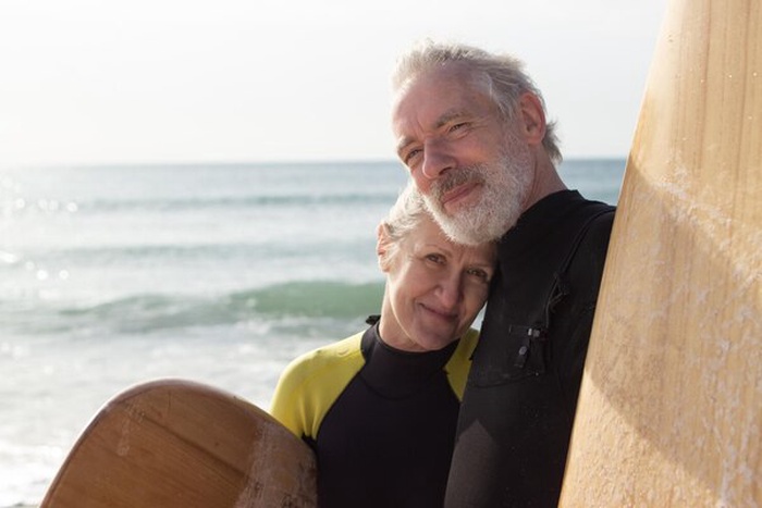 Portrait of happy senior couple with surfboards near sea