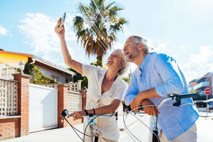 Joyful senior couple with bikes taking sunny outdoor selfie, active mature pair enjoying casual daytime date