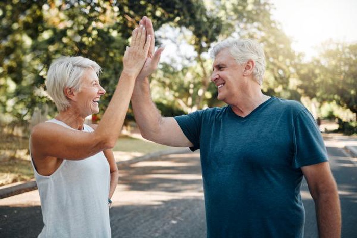 Happy mature couple high‑fiving outside in the park