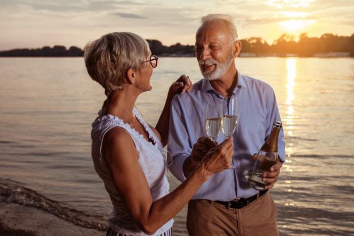 Senior couple toasting wine smiling at sunset beach