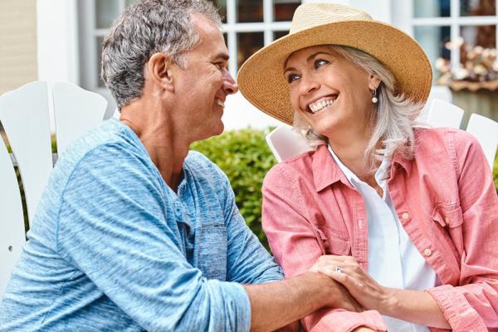 Happy middle-aged man and woman gazing affectionately while sitting outside