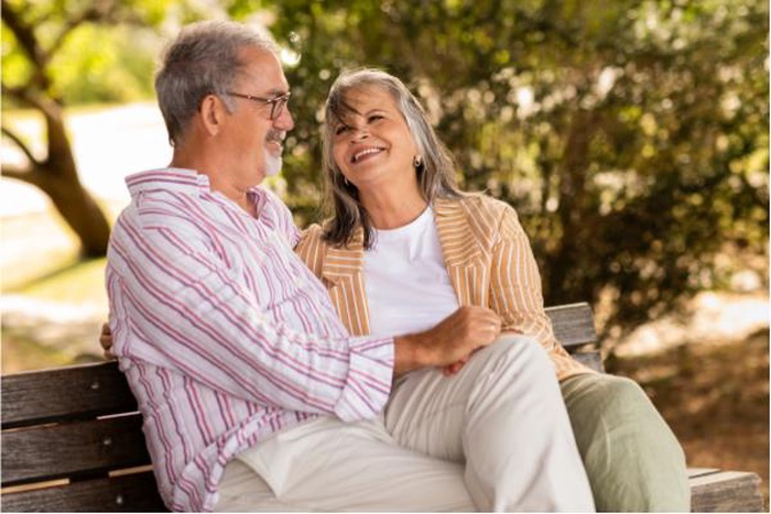 Affectionate senior couple laughing together on a park bench