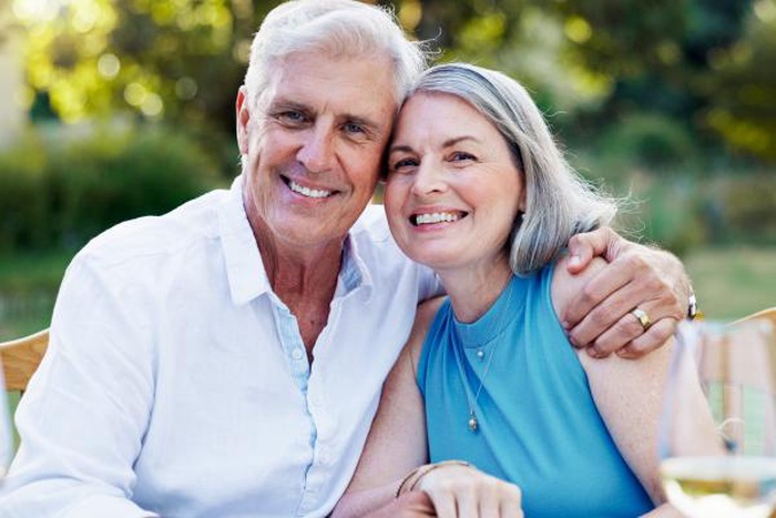 Smiling affectionate senior couple posing together outdoors at garden table