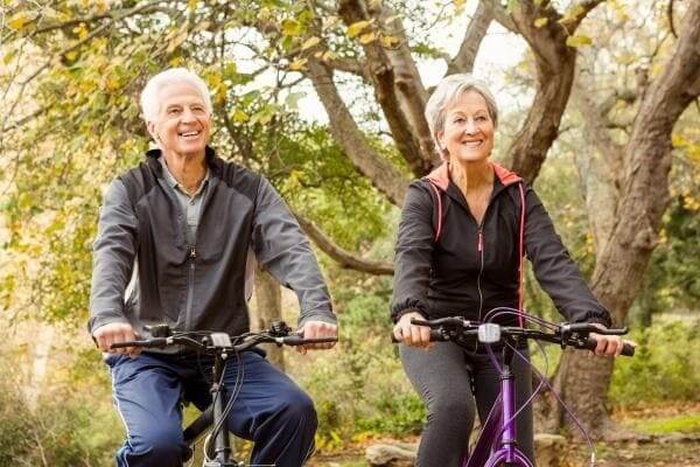 Happy elderly man and woman cycling outdoors, wholesome mature singles activity