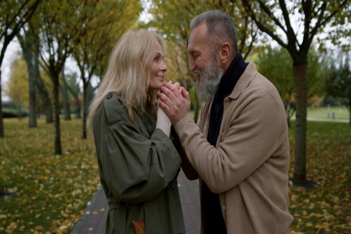 Closeup view of beautiful adult couple kissing hands of each other in romantic autumn atmosphere beautiful mature lovers having walk in daytime happy man enjoying of woman beauty in fall park