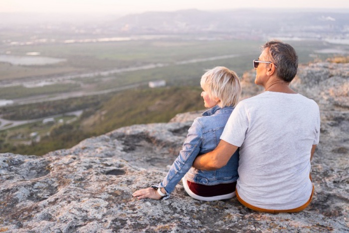 Full shot traveling couple sitting on cliff