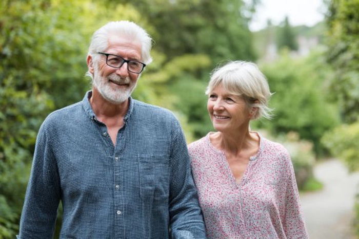 Deux seniors souriants se promenant ensemble sur un sentier dans un parc verdoyant.