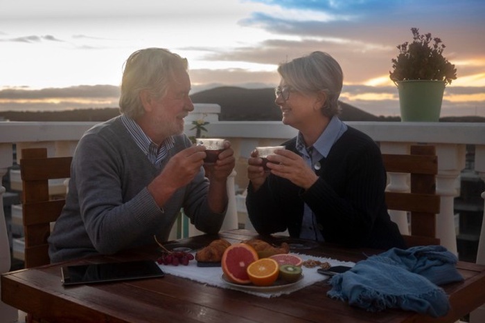 Senior man and woman with drinks sitting at table during sunset