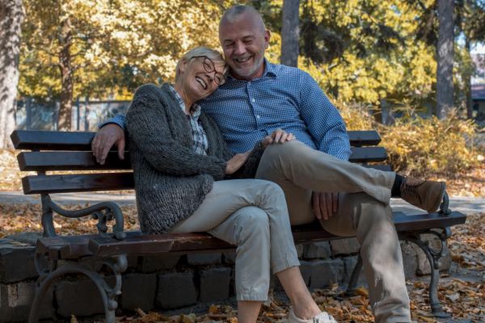 Laughing mature couple cuddling together on an autumn park bench