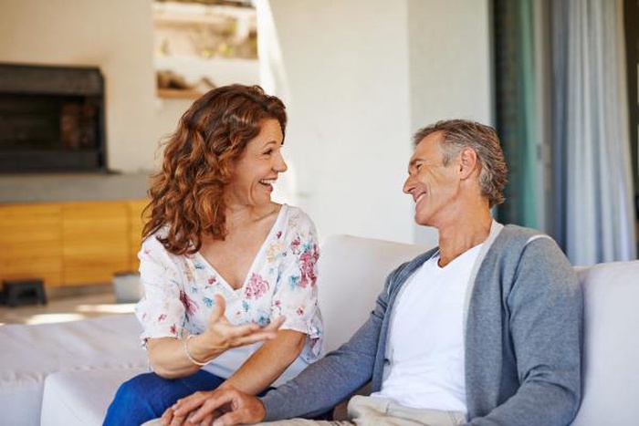 Joyful mature couple chatting and laughing while holding hands on a sofa at home