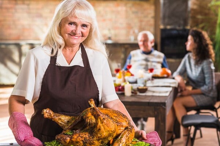 senior woman in pinafore holding plate with baked ham
