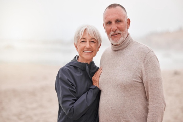 Portrait of happy and senior couple couple enjoy a romantic date at the beach on a misty day love happiness and elderly retired husband hug wife while seaside retirement vacation or travel holiday