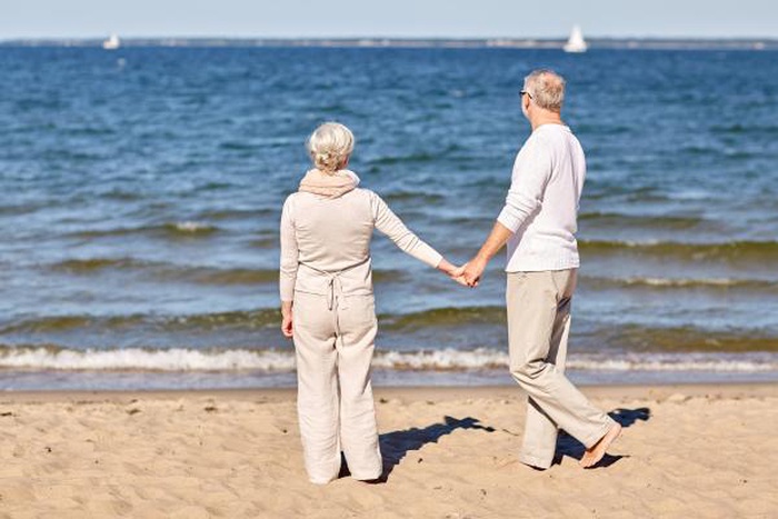 Mature senior couple holding hands walking on coastal beach, local over 50 singles find companionship and mature dating across USA and Europe