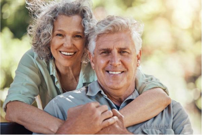 Happy affectionate mature Caucasian senior couple embracing warmly on an outdoor park bench