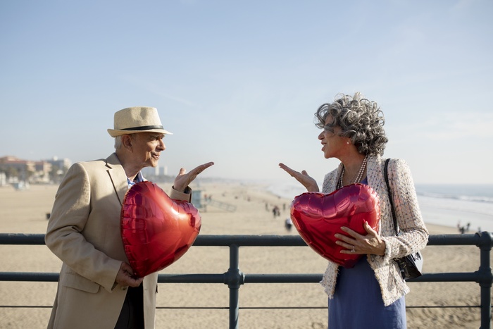  Senior couple sending air kisses to each other while holding heart-shaped balloons on a date