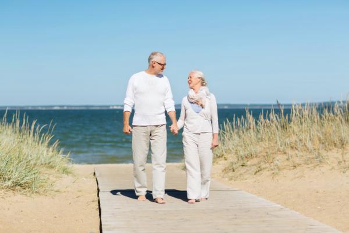 happy senior couple holding  hands and walking on summer beach