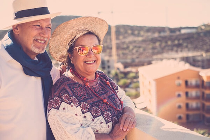 Casal de idosos sorridentes de p&eacute; no terra&ccedil;o do pr&eacute;dio