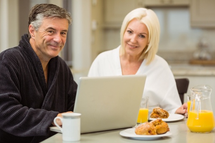 Mature couple having breakfast together man using laptop