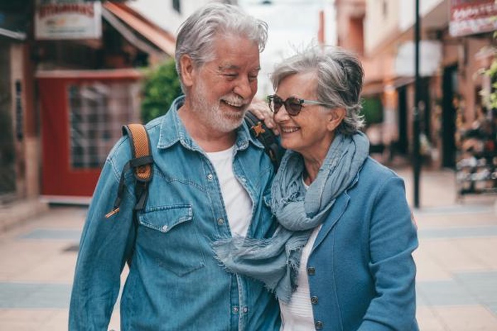 Cheerful elderly couple walking arm in arm downtown, happy mature pair traveling together, warm companionship for singles over 50