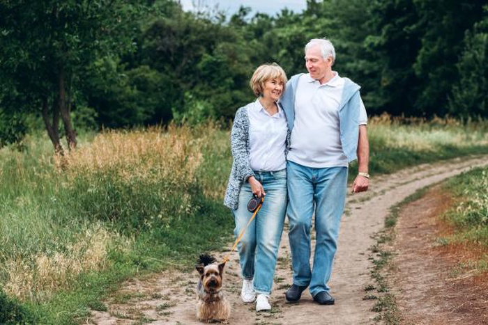 Mature couple is walking with dog in park