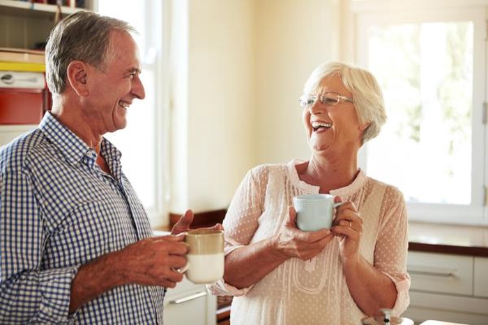 Joyful senior couple laughing together with mugs in the kitchen