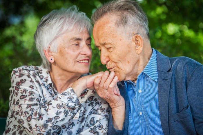 Head and shoulder view of elderly retired couple kissing hand against green blurred background