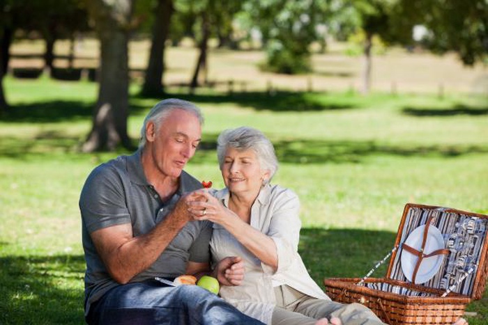 A senior couple happily eats fruit in the park