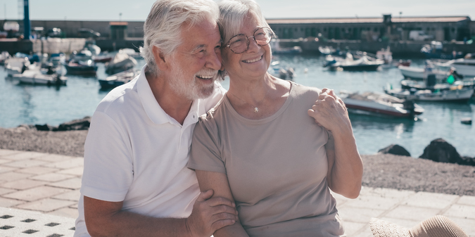 happy carefree senior couple embracing sitting together bench harbor