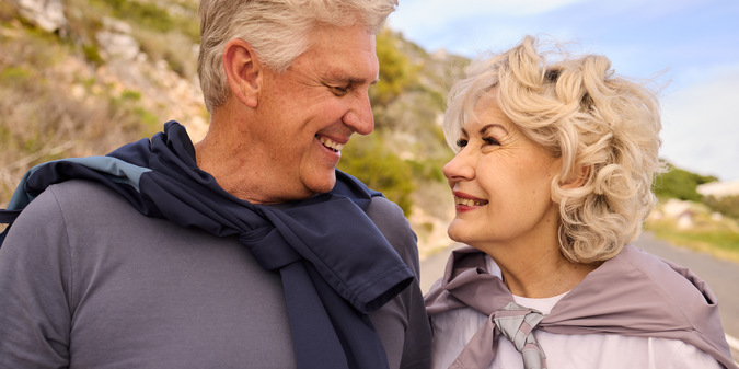 Two elderly people looked at each other affectionately and smiled in front of a mountain.