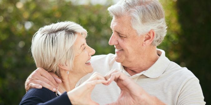Happy senior couple forming a heart with their hands, showing affection and confidence in their dating makeover journey.