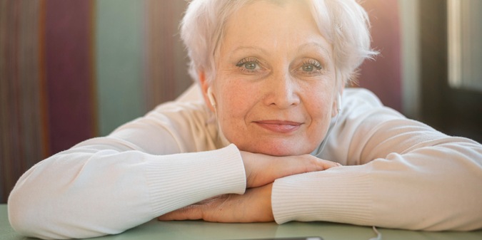 Senior female sitting with head on table and listening music
