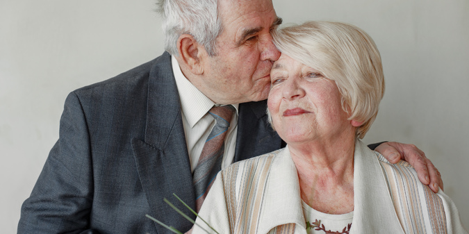 happy-elderly-couple-embracing-against-grey-wall