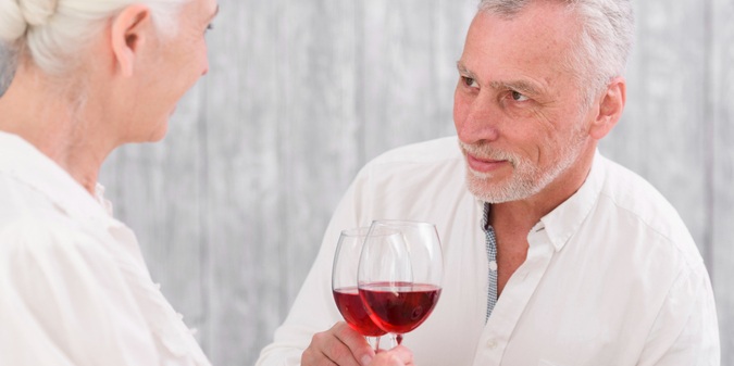 Senior smiling man clicking wine glass while looking his wife