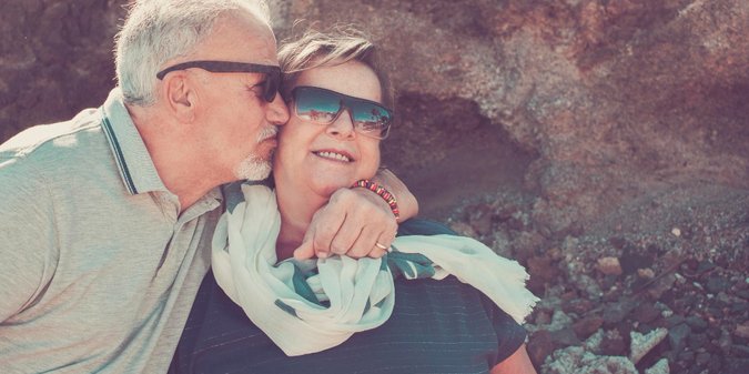 Senior man kissing woman sunglasses against rock